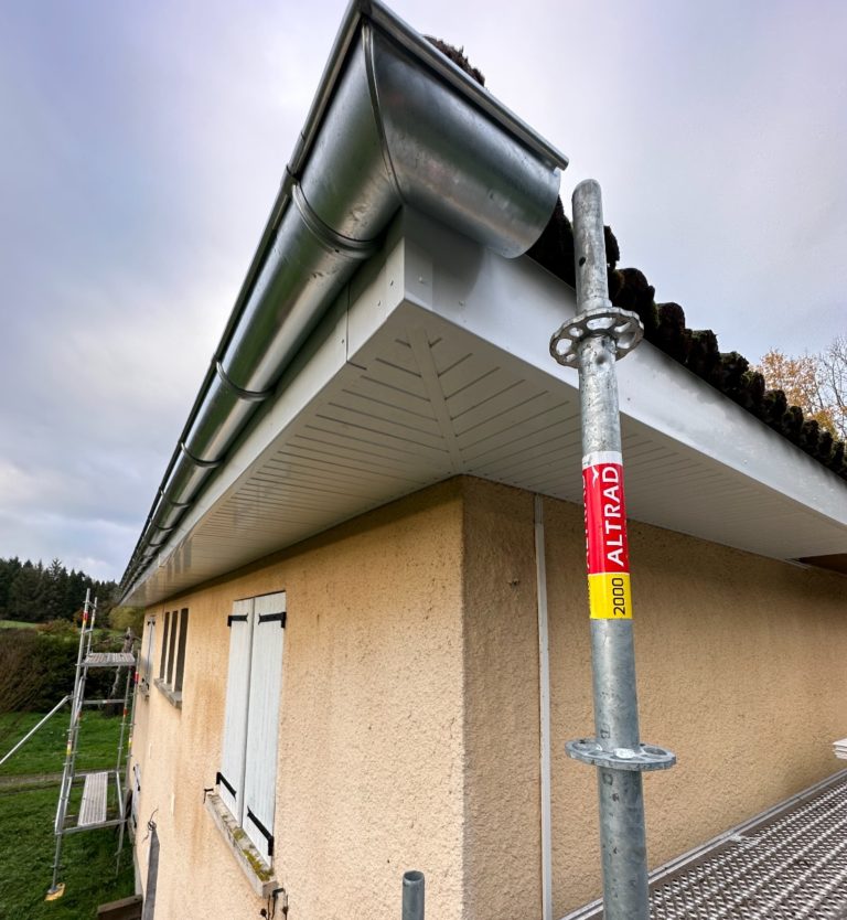 Avant-toit avec sous-faces PVC ajourées et gouttière zinc sur maison crépie, vue en contre-plongée.
