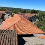 Toiture en tuiles rouges rénovée à Limoges par DGC Couverture, avec une vue panoramique sur les maisons environnantes et la campagne verdoyante.