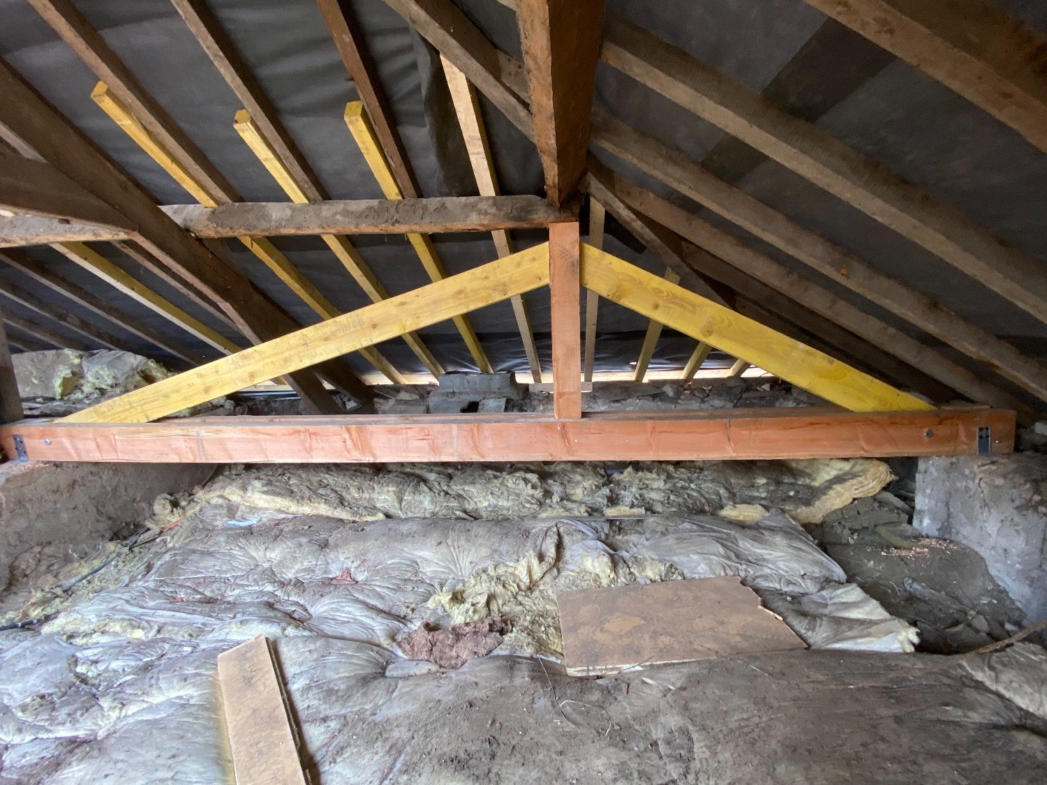 Vue d’un grenier montrant une charpente en bois rénovée avec des renforts en bois clair et des éléments isolants présents sur le sol.
