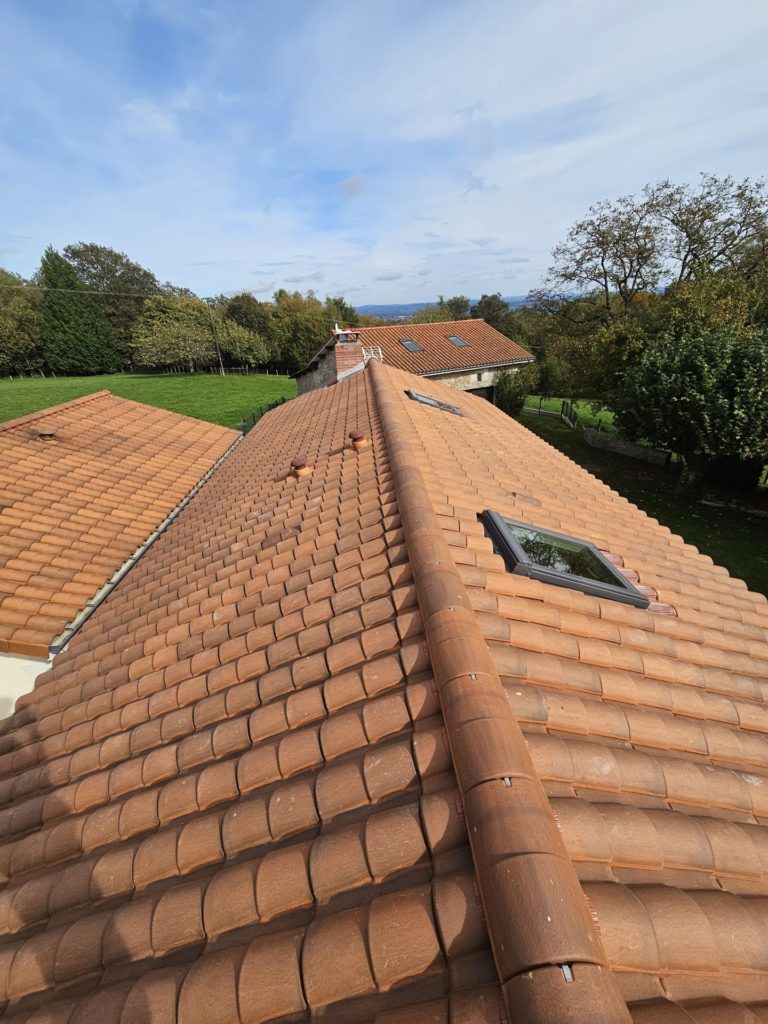 Vue aérienne d'une toiture en tuiles neuves de couleur terre cuite, réalisée à Limoges, avec des finitions impeccables, une fenêtre de toit et un cadre verdoyant à l'arrière-plan.