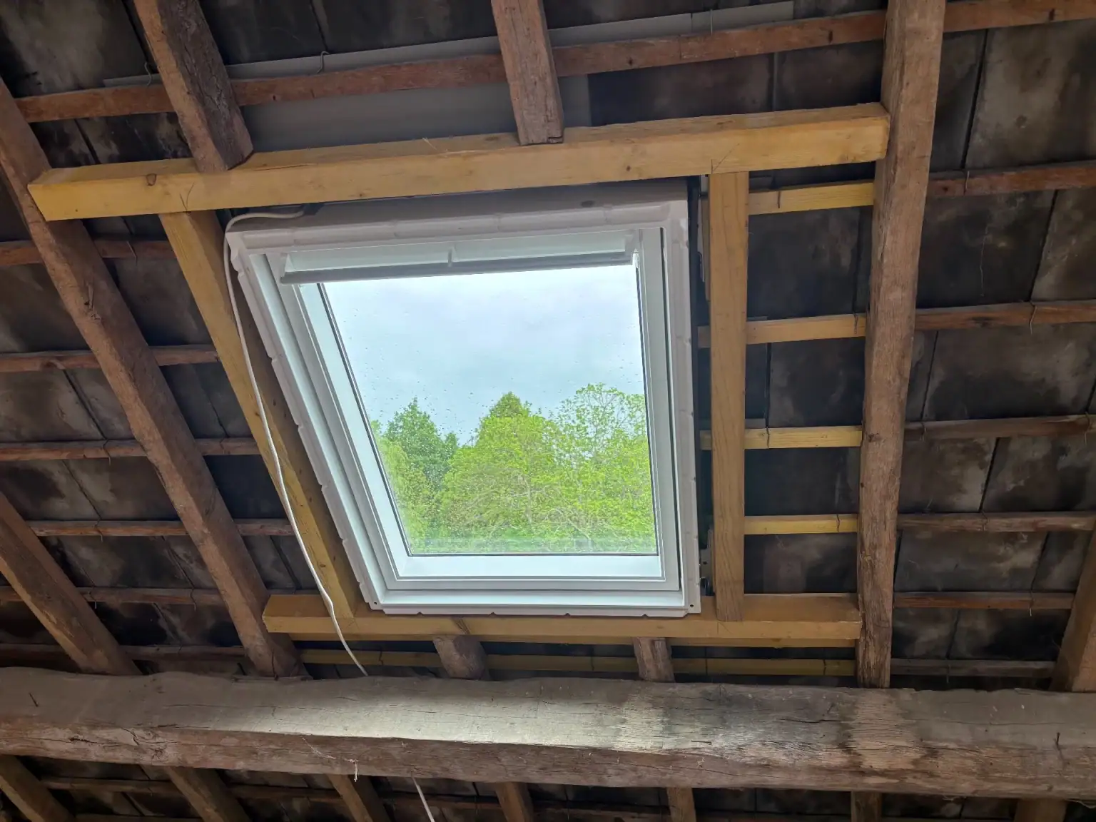 Fenêtre de toit installée sur une toiture existante à Limoges, avec encadrement bois et charpente apparente.