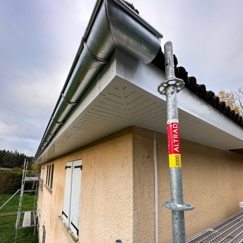 Avant-toit avec sous-faces PVC ajourées et gouttière zinc sur maison crépie, vue en contre-plongée.